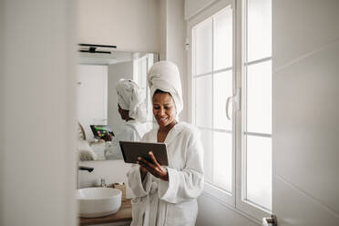 Glückliche reife Frau benutzt Tablet-PC im Badezimmer zu Hause - EBBF07904