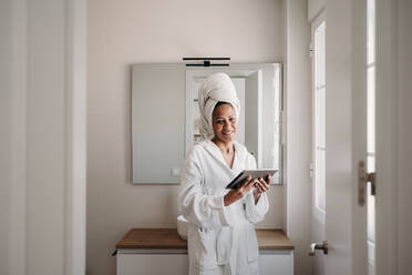 Smiling mature woman standing with tablet PC at home - EBBF07906