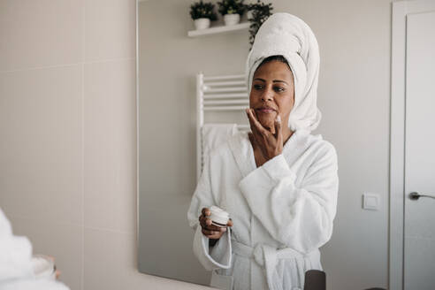 Ältere Frau trägt im Badezimmer Feuchtigkeitscreme auf das Gesicht auf - EBBF07910