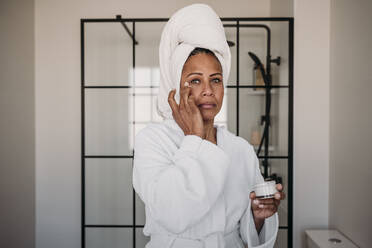 Frau trägt im Badezimmer zu Hause Feuchtigkeitscreme auf das Gesicht auf - EBBF07911