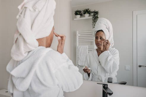 Reife Frau trägt im Badezimmer zu Hause Feuchtigkeitscreme auf das Gesicht auf - EBBF07914