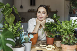 Lächelnde Frau, die sich bei frischen Pflanzen zu Hause auf die Ellbogen stützt - VBUF00235