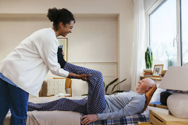 Fröhliche Physiotherapeutin hilft älterem Mann bei der Physiotherapie zu Hause - EBSF02671