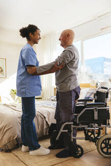 Physiotherapeutin unterstützt älteren Mann beim Stehen zu Hause - EBSF02682