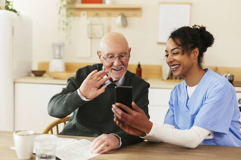 Hausmeister hält Smartphone für älteren Mann, der bei Videoanruf zu Hause winkt - EBSF02698