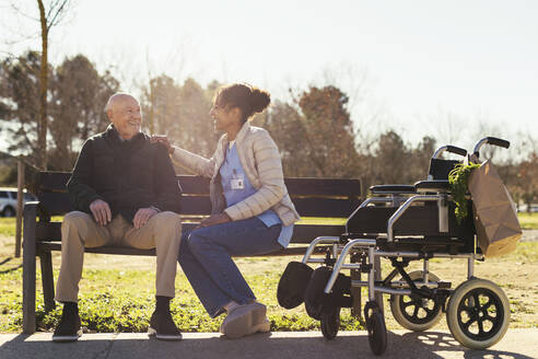 Smiling caretaker sitting with senior man in park - EBSF02701