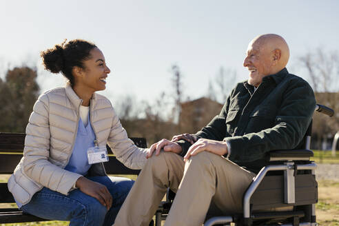 Glücklicher Hausmeister mit einem älteren Mann im Rollstuhl im Park - EBSF02704