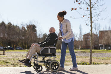 Woman assisting senior man on wheelchair in park - EBSF02706