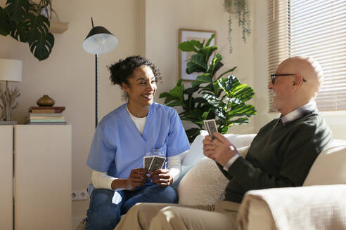 Happy senior man playing cards with caretaker at home - EBSF02708