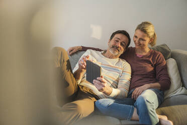 Couple sharing tablet PC sitting on sofa at home - JOSEF16639