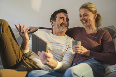 Happy couple with tablet PC enjoying on sofa at home - JOSEF16643