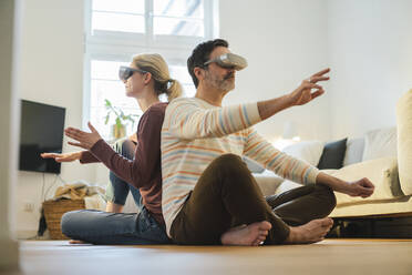 Mature couple wearing wearing virtual reality headset and gesturing at home - JOSEF16644