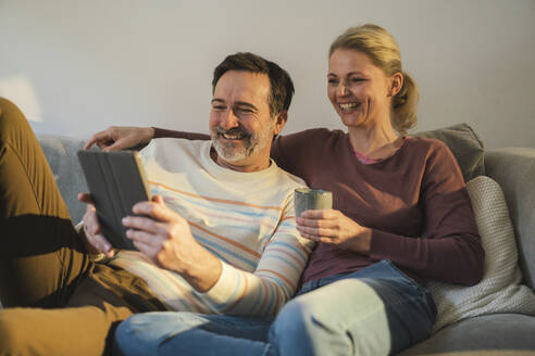 Glückliches reifes Paar, das zu Hause auf dem Sofa sitzend einen Tablet-PC betrachtet - JOSEF16645