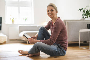 Happy woman with tablet PC sitting on floor at home - JOSEF16690