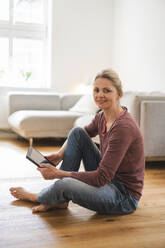 Lächelnde reife Frau mit Tablet-PC zu Hause sitzend - JOSEF16691