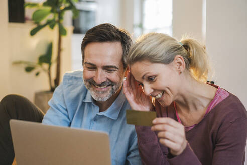 Happy couple doing online shopping through laptop at home - JOSEF16714