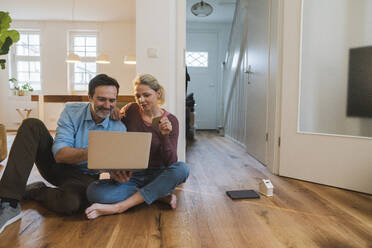 Mann und Frau beim Online-Shopping auf dem Boden sitzend zu Hause - JOSEF16747