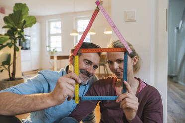 Ehemann und Ehefrau halten ein Hausmodell aus Zollstock zu Hause - JOSEF16753