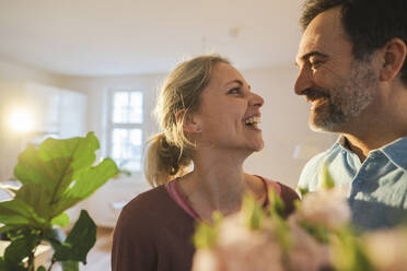 Happy romantic mature couple looking at each other in front of flowers - JOSEF16756