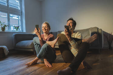 Lächelndes Paar mit Mobiltelefonen übt Yoga zu Hause - JOSEF16794