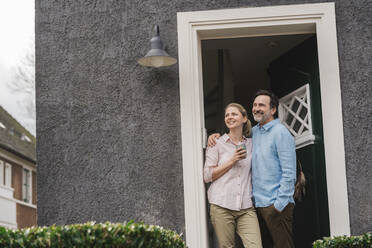 Smiling mature couple day dreaming at doorway of house - JOSEF16800