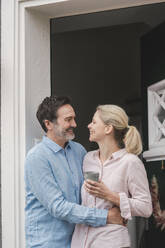 Glücklicher Mann, der seine Frau mit einer Tasse umarmt, am Eingang eines Hauses - JOSEF16802