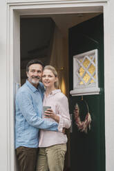 Älterer Mann umarmt seine Frau und hält eine Tasse in der Tür eines Hauses - JOSEF16804