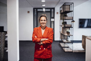 Smiling businesswoman wearing orange blazer in office - JOSEF16817