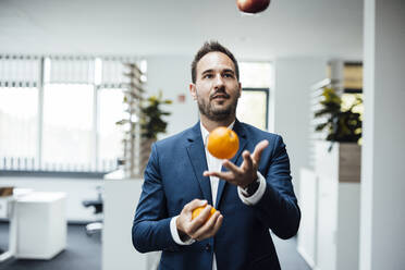 Geschäftsmann jongliert Orangen im Büro - JOSEF16856
