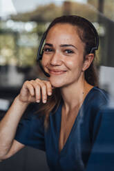 Smiling businesswoman wearing headset seen through glass - JOSEF16881