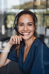 Happy businesswoman wearing headset sitting in soundproof cabin - JOSEF16882