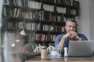 Freiberufler mit Laptop sitzt am Tisch in einem Cafe - KNSF09620