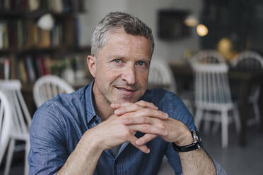 Smiling man with hands clasped sitting at cafe - KNSF09621