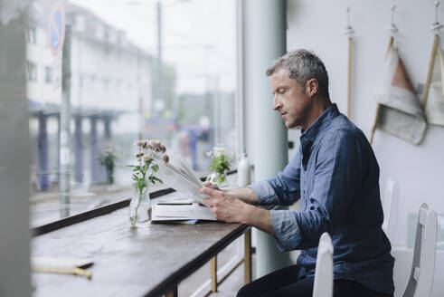 Businessman reading newspaper sitting in cafe - KNSF09626