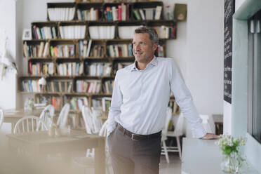 Smiling businessman with hand in pocket leaning at cafe - KNSF09627