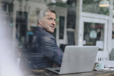 Lächelnder Geschäftsmann mit Laptop durch Glas gesehen - KNSF09632