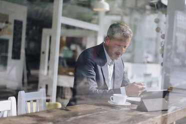 Businessman having breakfast and using tablet PC at cafe - KNSF09640