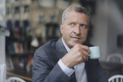 Nachdenklicher reifer Geschäftsmann mit Kaffeetasse durch Glas gesehen - KNSF09648