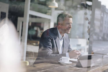 Mature businessman having breakfast seen through glass in cafe - KNSF09651