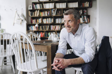 Happy thoughtful businessman sitting on chair in cafe - KNSF09654