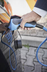 Hand eines jungen Geschäftsmannes, der sein Auto an einer Elektrofahrzeug-Station auflädt - RORF03342