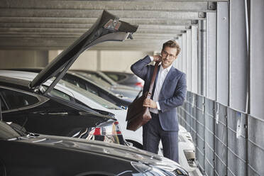 Businessman standing with shoulder bag in parking garage - RORF03343