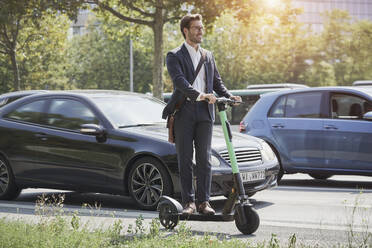 Lächelnder Geschäftsmann auf einem elektrischen Roller auf der Straße stehend - RORF03344