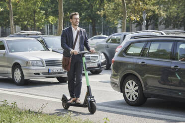 Lächelnder junger Geschäftsmann auf einem elektrischen Roller auf der Straße stehend - RORF03345