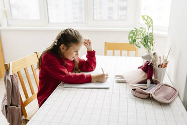 Girl sitting at table doing home work - SSYF00081