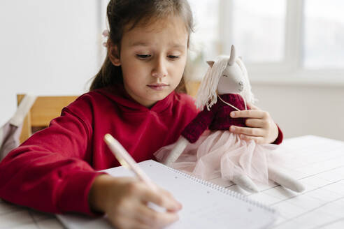 Mädchen mit Einhornspielzeug beim Lernen zu Hause - SSYF00087