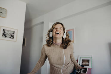 Glückliche Frau mit Kopfhörern beim Musikhören zu Hause - DMGF01024