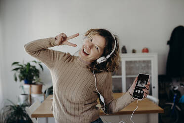 Carefree woman wearing headphones enjoying music and dancing at home - DMGF01025