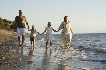 Familie hält sich an den Händen und geht am Strand spazieren - NJAF00207
