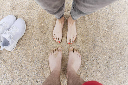 Man and woman standing barefeet on sand at beach - CHPF00860